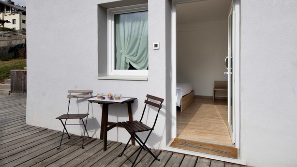 Una habitación pequeña con una cama, una mesa con sillas y un ventanal con cortina.
