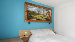 Una cama individual con tablero de madera, una mesita de noche y un cuadro colgado en la pared que muestra un paisaje montañoso.