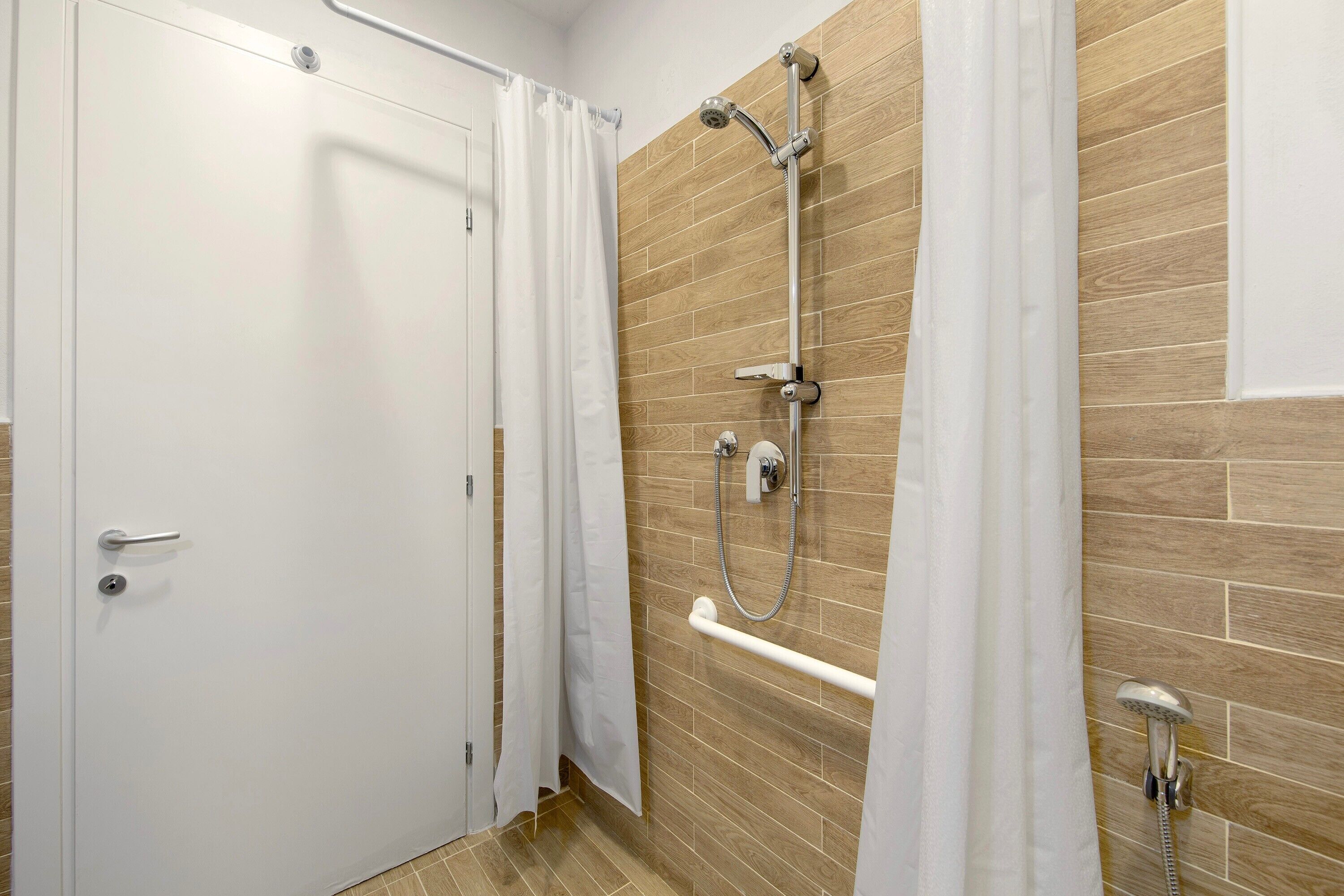 Un baño con ducha, una puerta blanca y un muro de madera.