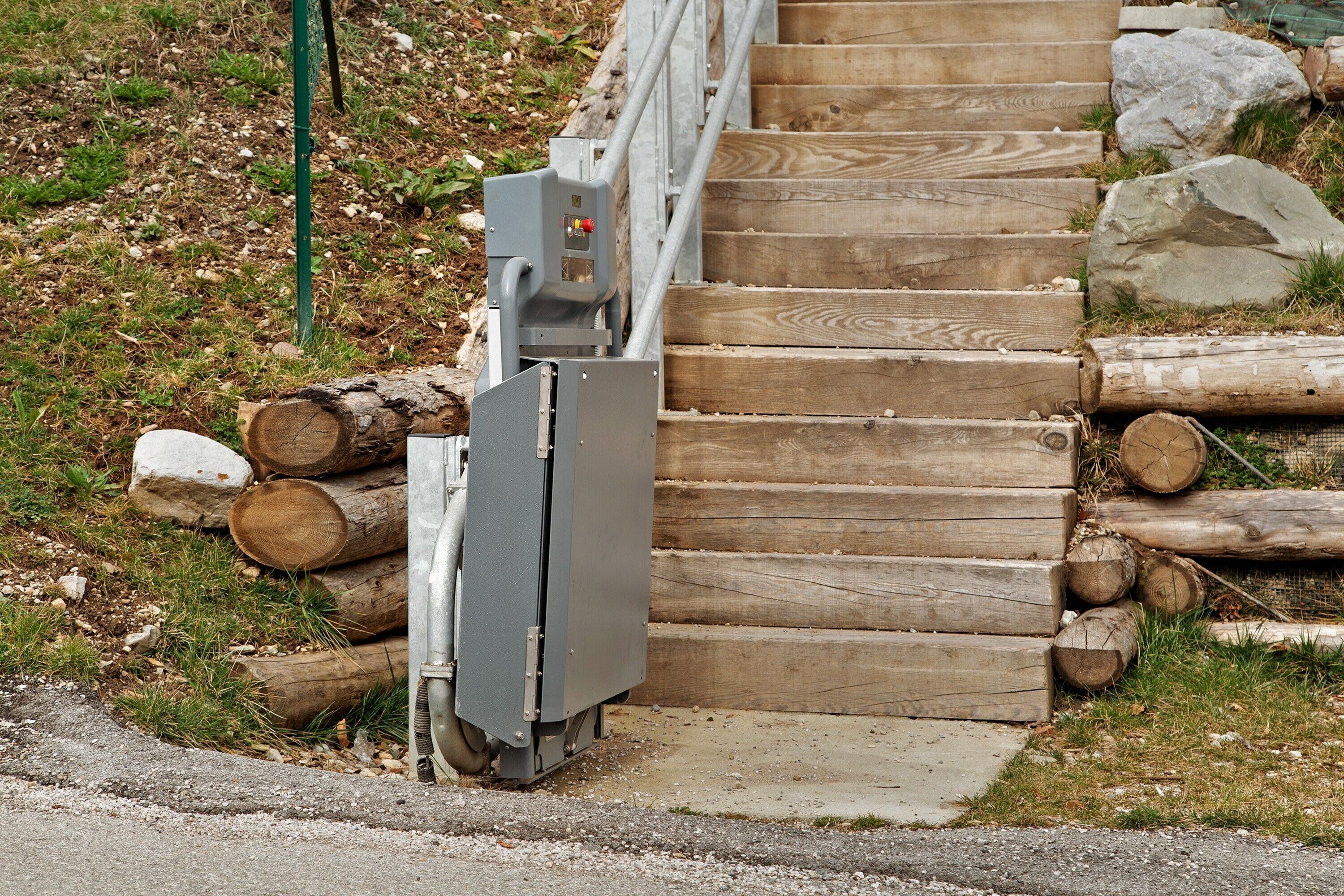 Eine Holztreppe mit Metallgeländer, umgeben von Baumstämmen und einem grünen Pfosten.