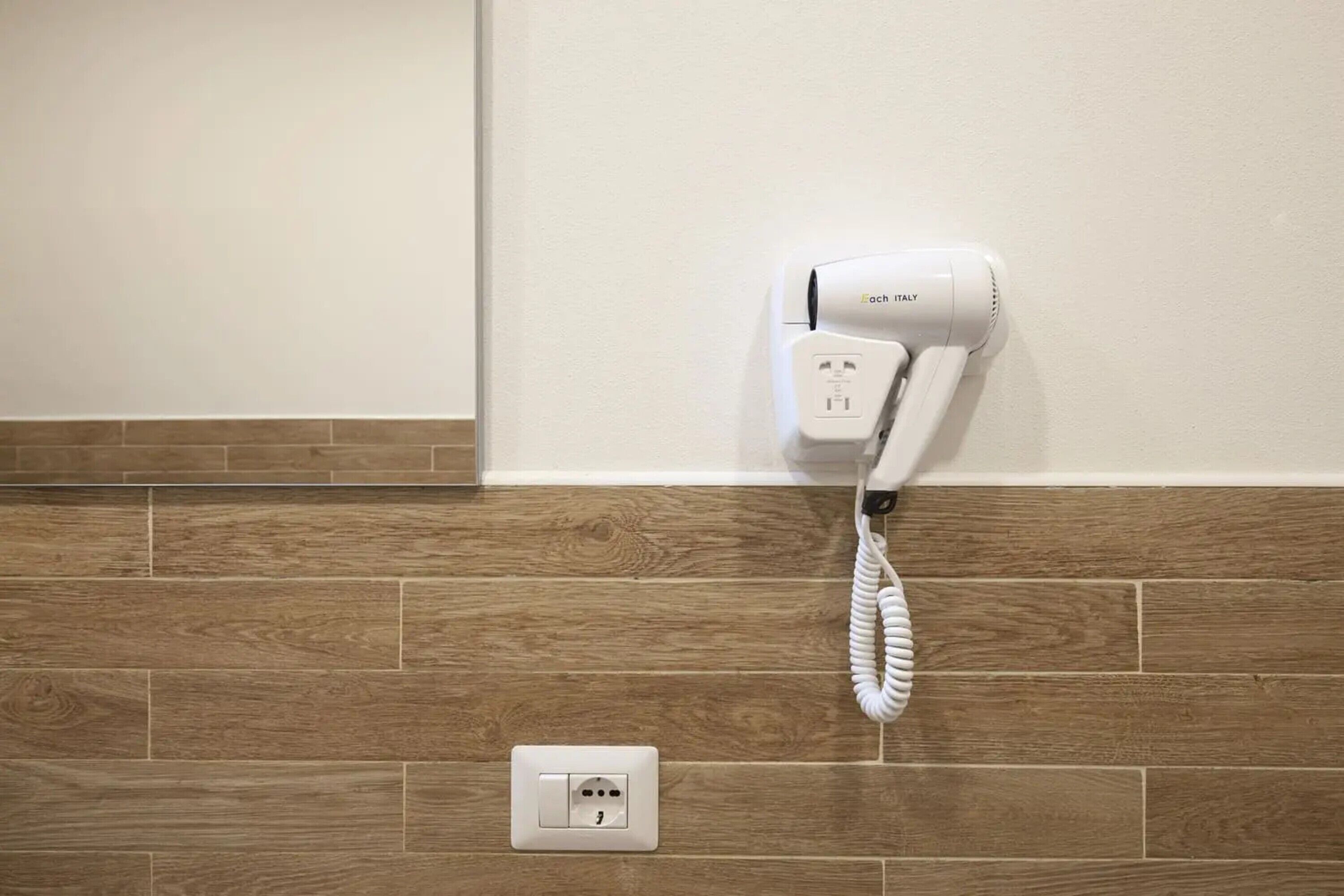 Un secador de pelo fijado a la pared, con suelo de madera y pared blanca.