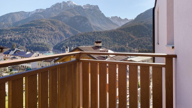 Un balcon donnant sur une chaîne de montagnes, un bâtiment doté d’un toit en pente et un ciel dégagé.