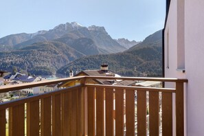 Ein Balkon mit Blick auf ein Gebirge, ein Gebäude mit schrägem Dach und einem klaren Himmel.