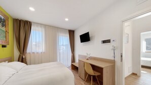 Une chambre d’hôtel avec un lit, un bureau, une chaise, une télévision et une fenêtre avec des rideaux.