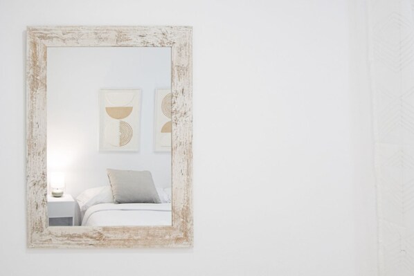 A bedroom with a bed, a nightstand, and a wall-mounted mirror with a distressed frame.