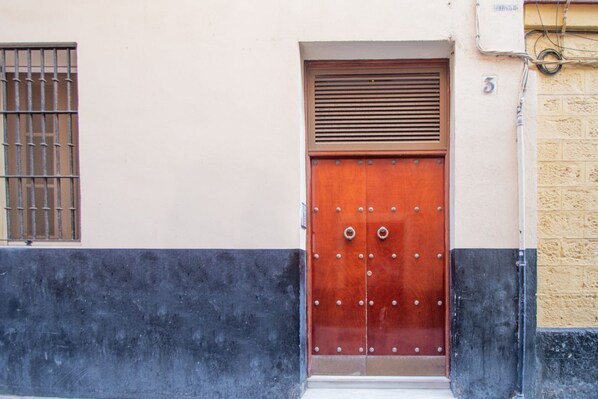 Una puerta de madera con remaches metálicos y un ventanal con barrotes.