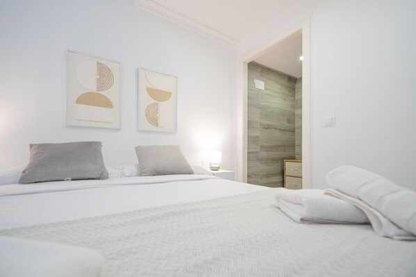 A modern bedroom with a large bed, two pillows, a bedside table, and a nightstand. There are abstract wall art pieces above the bed.
