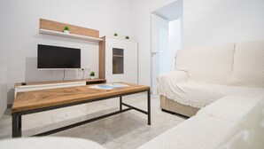 Een moderne woonkamer met een houten salontafel, een flatscreen televisie aan de muur, een witte bank en een klein plantje op een plank.