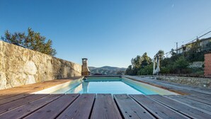 A wooden deck with a pool, stone walls, and a view of distant hills.
