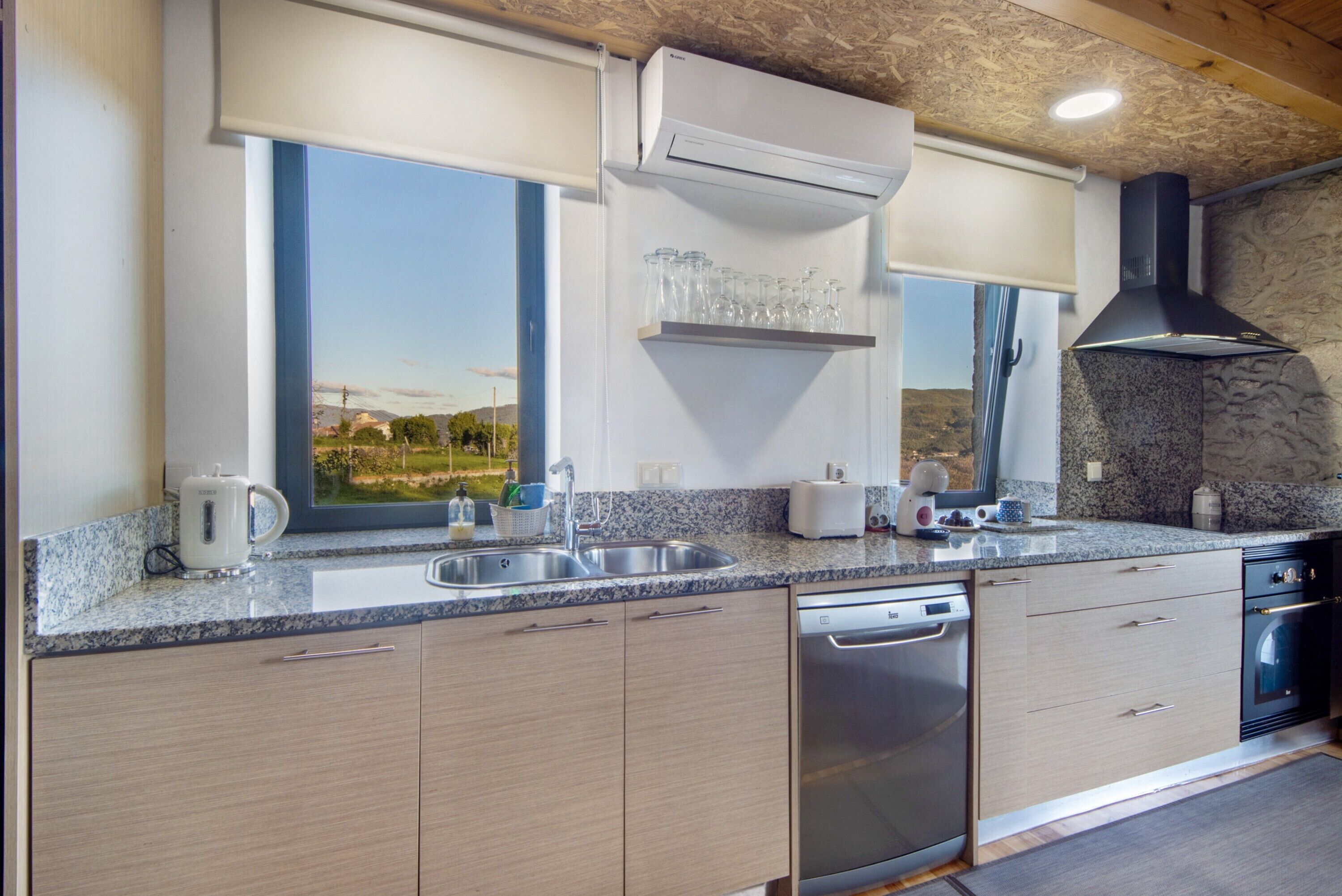 Una cucina moderna con lavastoviglie, doppio lavello e finestra vista campagna.