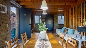 A wooden interior with a dining table, chairs, a sofa, and a vase with flowers.