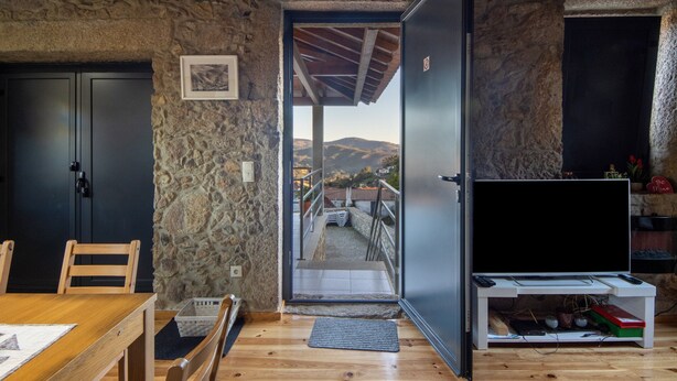 A room with a stone wall, a wooden ceiling, a TV stand, and a view of a balcony with steps leading outside.