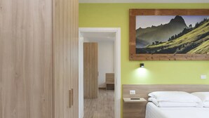 Ein Hotelzimmer mit einem Bett, einem Nachttisch, einem Holzschrank und einem Wandbild mit einer Berglandschaft.