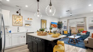 A modern kitchen with white cabinets, a central island, and a dining area with a blue sofa and yellow cushions. - Freedom Village 549, Smart TV, Private Balcony, Resort Amenities and more (Washington)