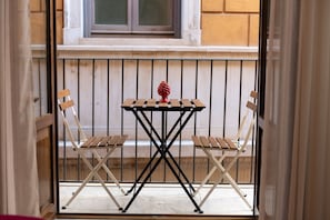 Ein Balkon mit einem kleinen Tisch und zwei Stühlen, einem dekorativen Gegenstand auf dem Tisch sowie Blick auf ein Gebäude im Hintergrund.
