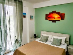 Una habitación con cama, mesita de noche, una obra de arte en la pared y una ventana con cortinas.
