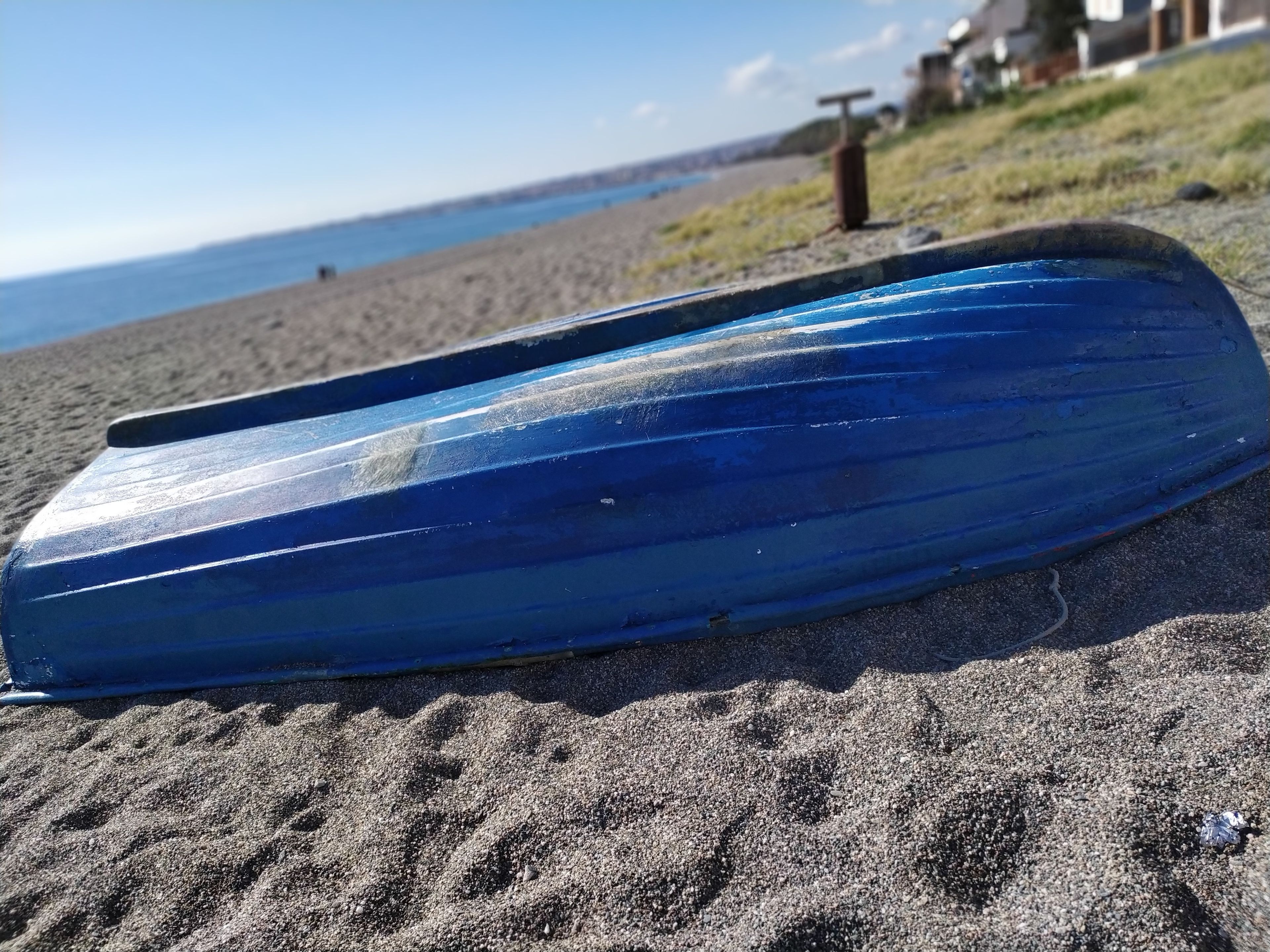 A blue boat on a sandy beach with a clear sky and distant buildings.
