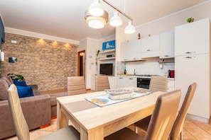 Une cuisine moderne avec des meubles blancs, une table à manger avec des chaises et un mur en pierre.
