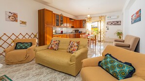Ein Wohnzimmer mit einer Couch, Sesseln, einer Küche im Hintergrund und einem Essbereich.