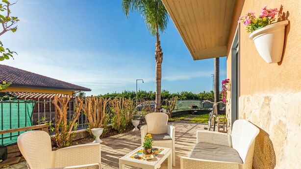 Eine Terrasse im Freien mit Korbmöbeln, einem Tisch mit Dekoration und einem hängenden Blumentopf.