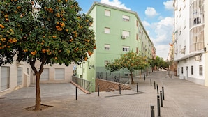 Une zone piétonne dallée, bordée d’arbres fruitiers, un bâtiment écologique doté de nombreuses fenêtres et un ciel dégagé.