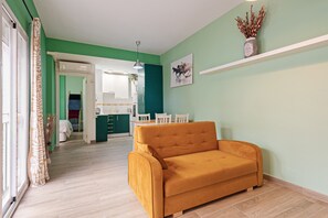 Una habitación con sofá, mesa de comedor, zona de cocina y un pasillo que conduce a otra habitación.