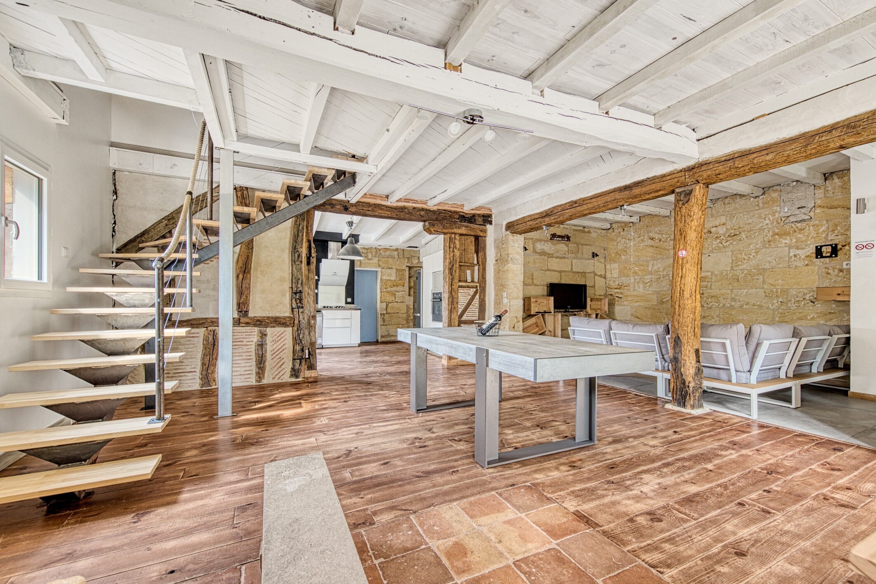 A spacious room with a wooden staircase, a dining table, and a seating area.