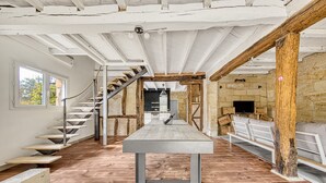 Ein geräumiger Raum mit einem langen Tisch, Holzboden, einer Treppe, Steinwänden und einem Fernseher.