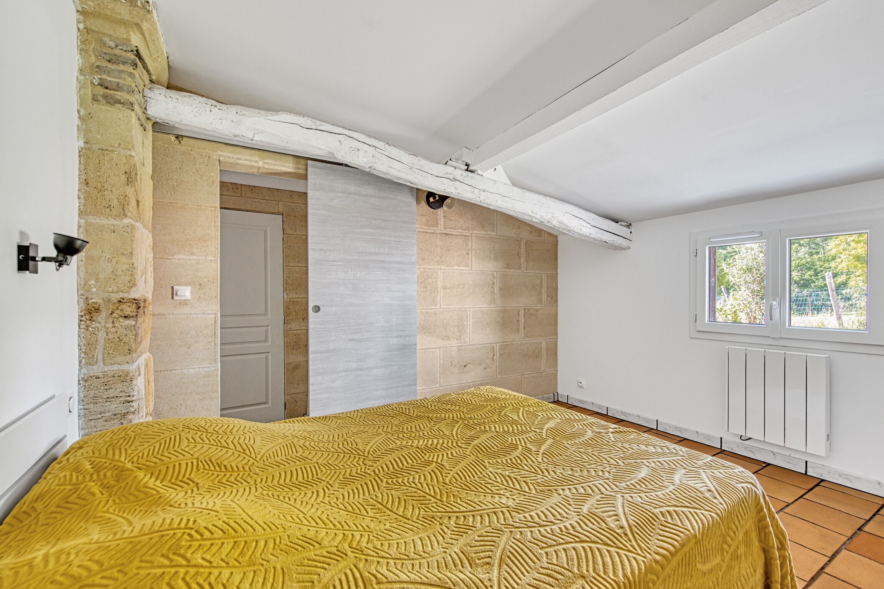 Une chambre à coucher avec un lit, une porte, une fenêtre et un mur en pierre.