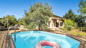 Ein Swimmingpool mit einem pinkfarbenen Donut-Schwimmreifen, umgeben von einer Holzterrasse und Bäumen.