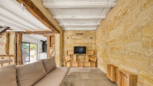 Ein gemütliches Zimmer mit Steinwand, Flachbildfernseher, Holzkisten und einem beigefarbenen Sofa.