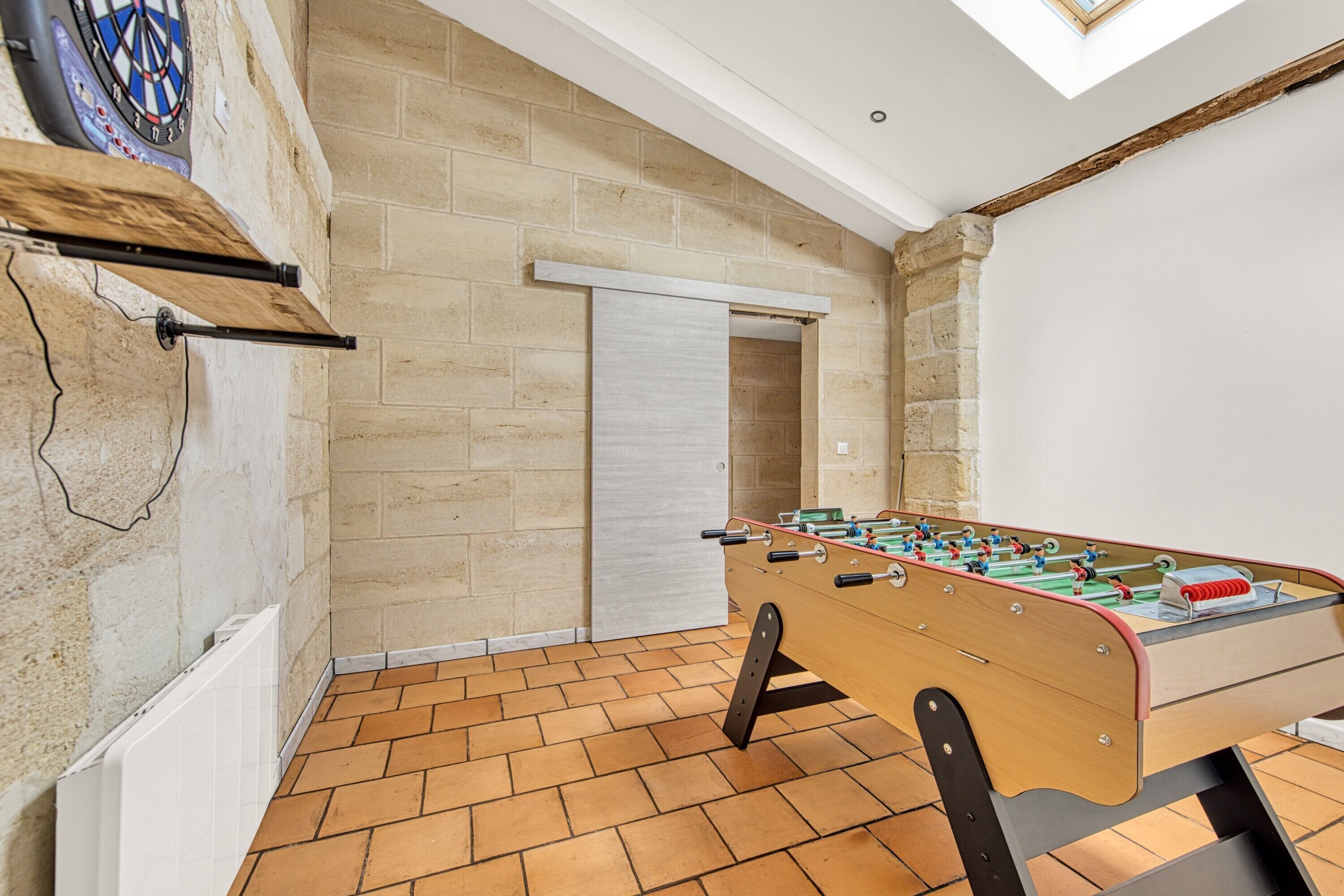 Una habitación con mesa de futbolín, dardos y un ventanal grande.