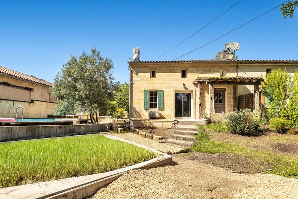 A stone building with a swimming pool, a garden, and a small staircase leading to the entrance.