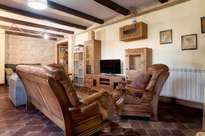 A living room with leather chairs, a TV, wooden cabinets, and a stone wall. - Country House 'Arroyo Del Valle' with Terrace and Private Garden (San Andrés del Rabanedo)