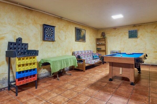 A room with a billiards table, a dartboard, a sofa, and a dartboard rack.