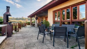 An outdoor patio with a grill, chairs, and a view of the countryside.