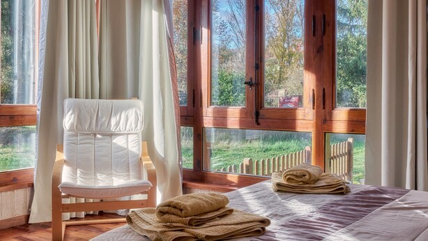 A bedroom with a bed, a chair, and a view of the outdoors.