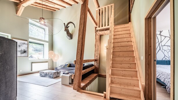 Un interno moderno con una scala in legno, un divano, un tavolo da pranzo e vista sull'esterno.