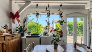 Un comedor con una mesa de madera, sillas, plantas colgantes y un adorno con lazo rojo.