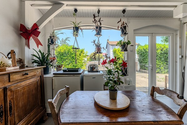 A dining area with a wooden table, chairs, hanging plants, and a red bow decoration.