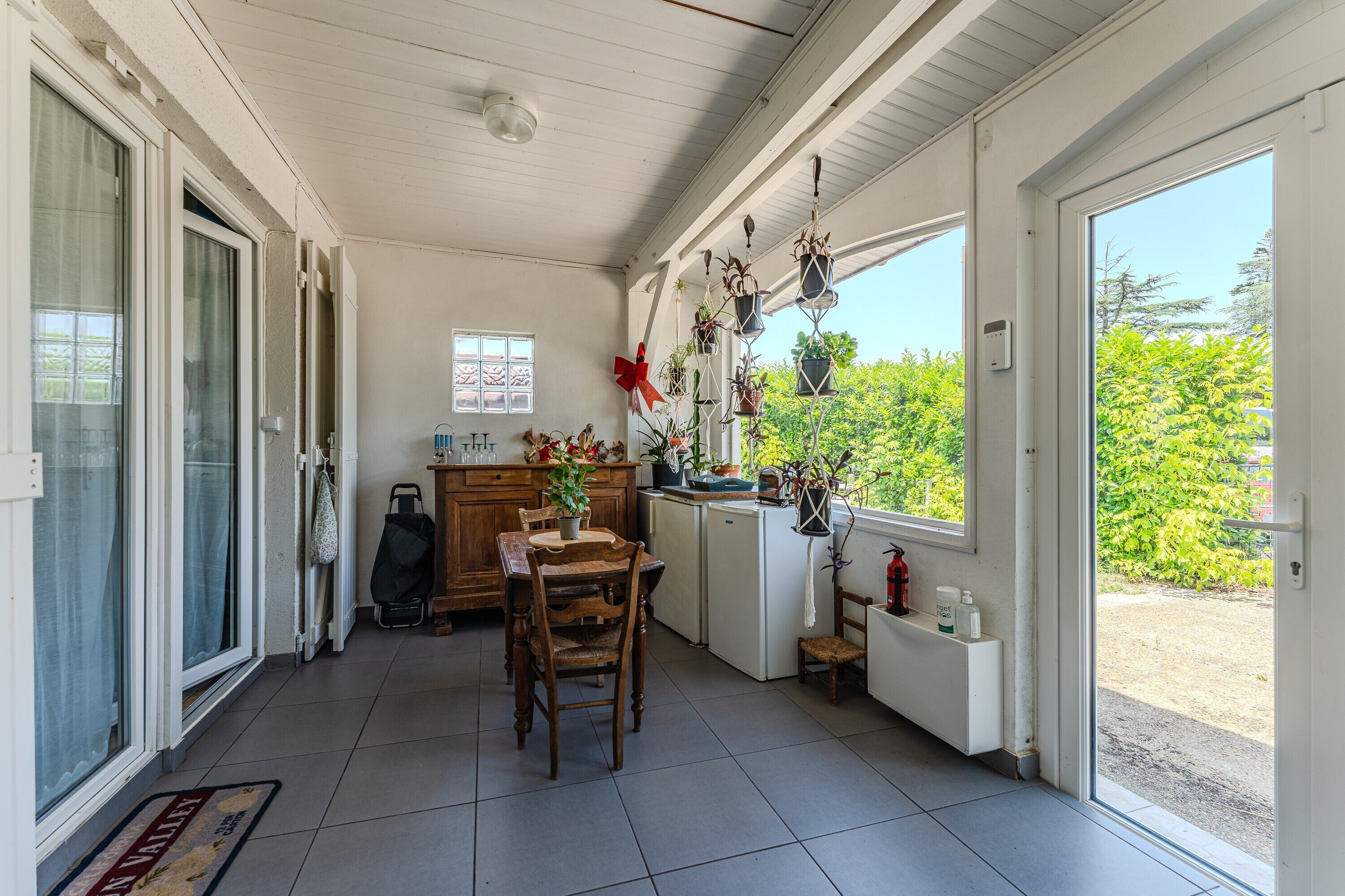 Une terrasse couverte avec une table à manger, des chaises, des plantes en pot et une vue sur la verdure environnante.