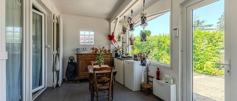 Une terrasse couverte avec une table à manger, des chaises, des plantes en pot et une vue sur la verdure environnante.