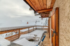 Un balcón de madera con barandillas cubiertas de nieve y vista a un paisaje nevado.