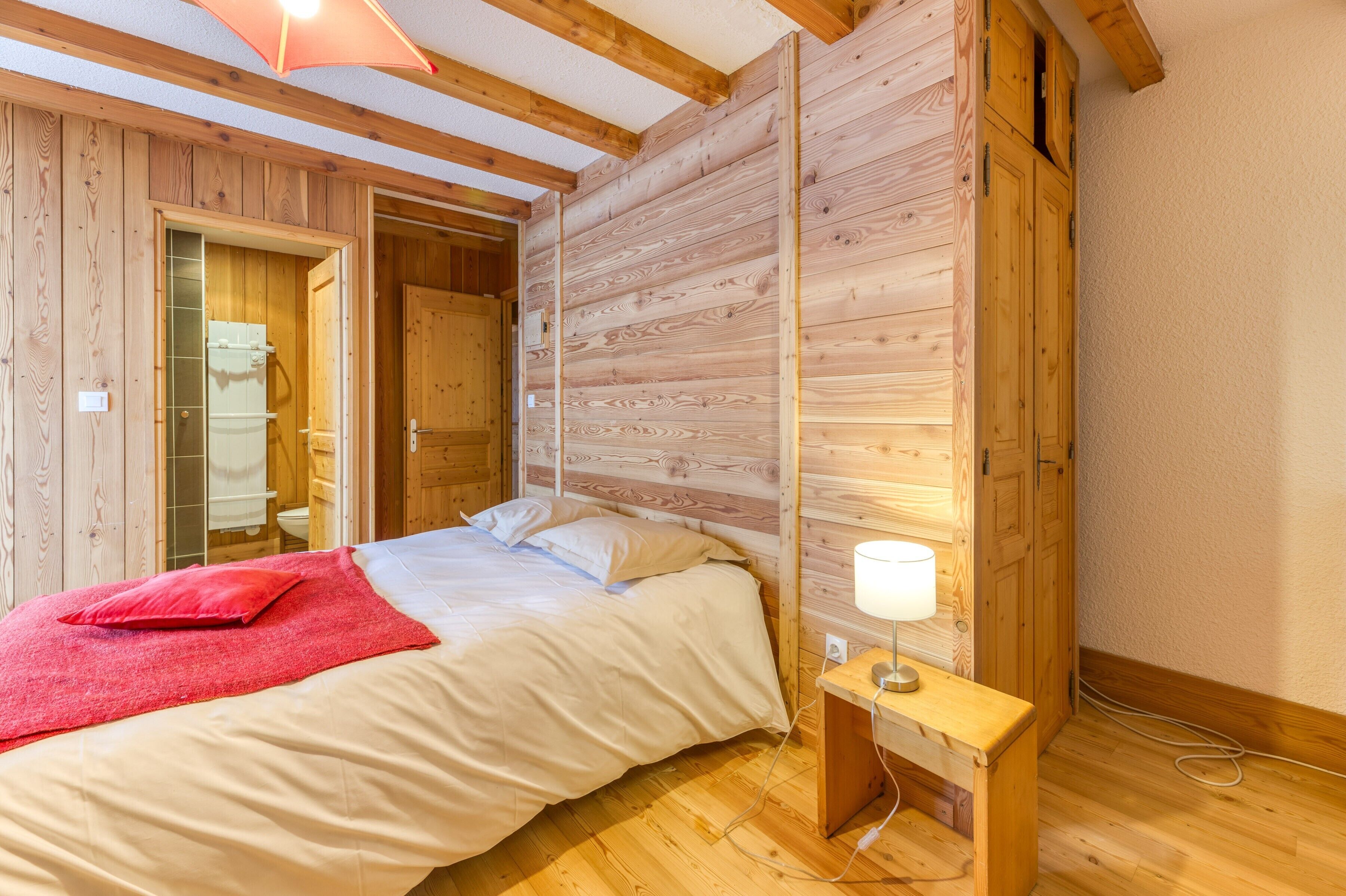 A wooden-paneled room with a bed, a bedside table with a lamp, and a wooden bench.