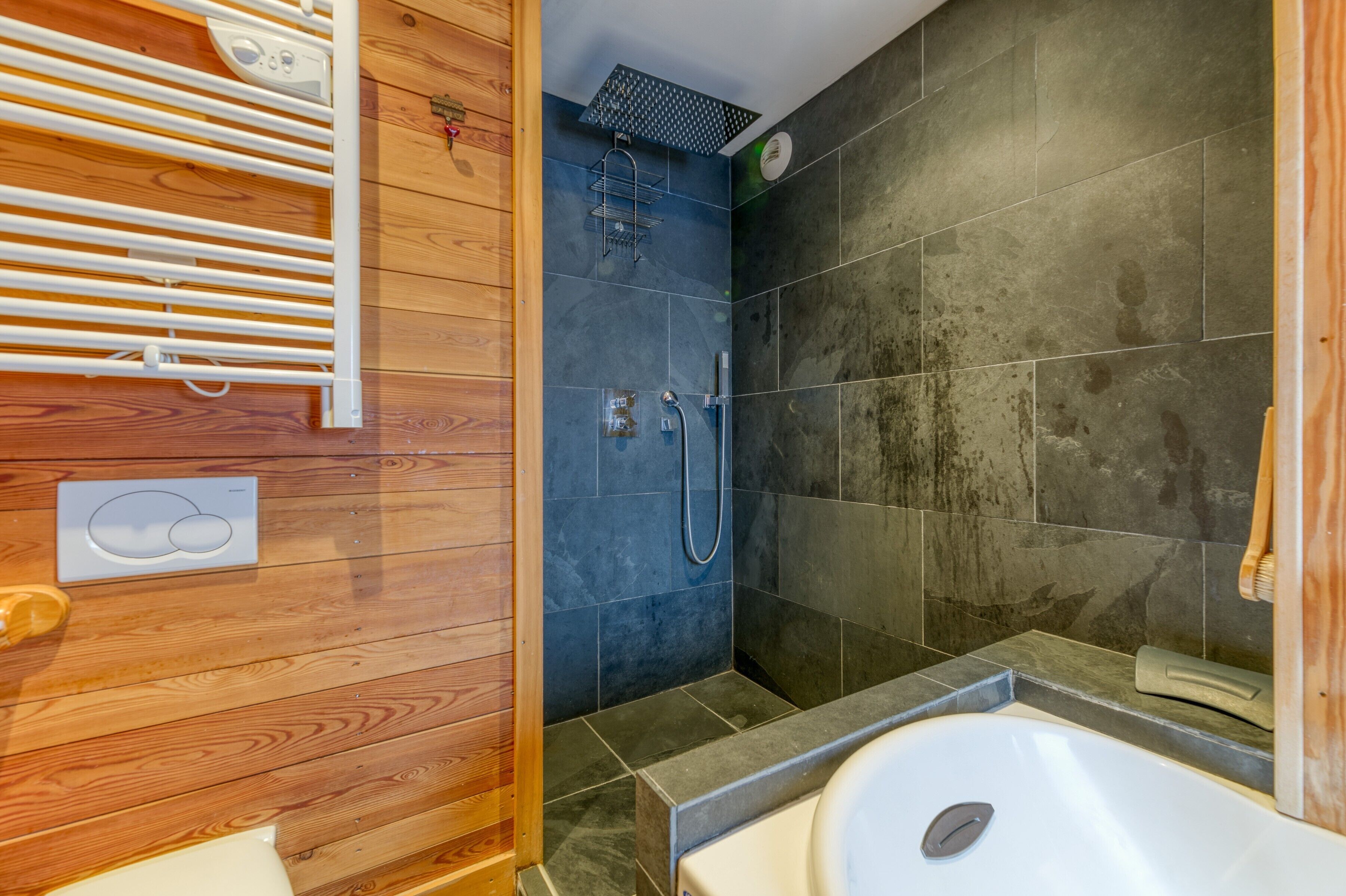 Ein Badezimmer mit einem Holzbadezimmermöbel, einer Badewanne, einer Dusche mit Regendusche und einem Handtuchhalter.
