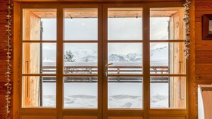 A wooden cabin with a large window offering a view of a snowy mountain landscape. - Chalet "Belledonne" with Mountain Views, Private Terrace and Wi-Fi (Villard-Reculas)
