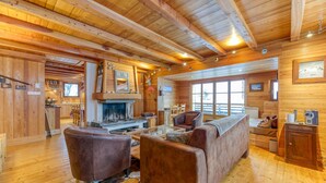 A log cabin interior with a fireplace, wooden furniture, and large windows. - Chalet "Belledonne" with Mountain Views, Private Terrace and Wi-Fi (Villard-Reculas)