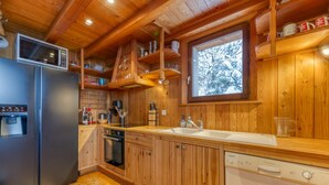 A wooden cabin kitchen with a refrigerator, dishwasher, and wooden cabinets. - Chalet "Belledonne" with Mountain Views, Private Terrace and Wi-Fi (Villard-Reculas)