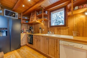 Une cuisine rustique, située dans une cabane en bois, équipée d’un réfrigérateur, d’un lave-vaisselle et de meubles de rangement en bois.