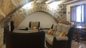 A stone archway leading to a cozy seating area with a sofa and armchairs, a wooden table, and a stone wall.
